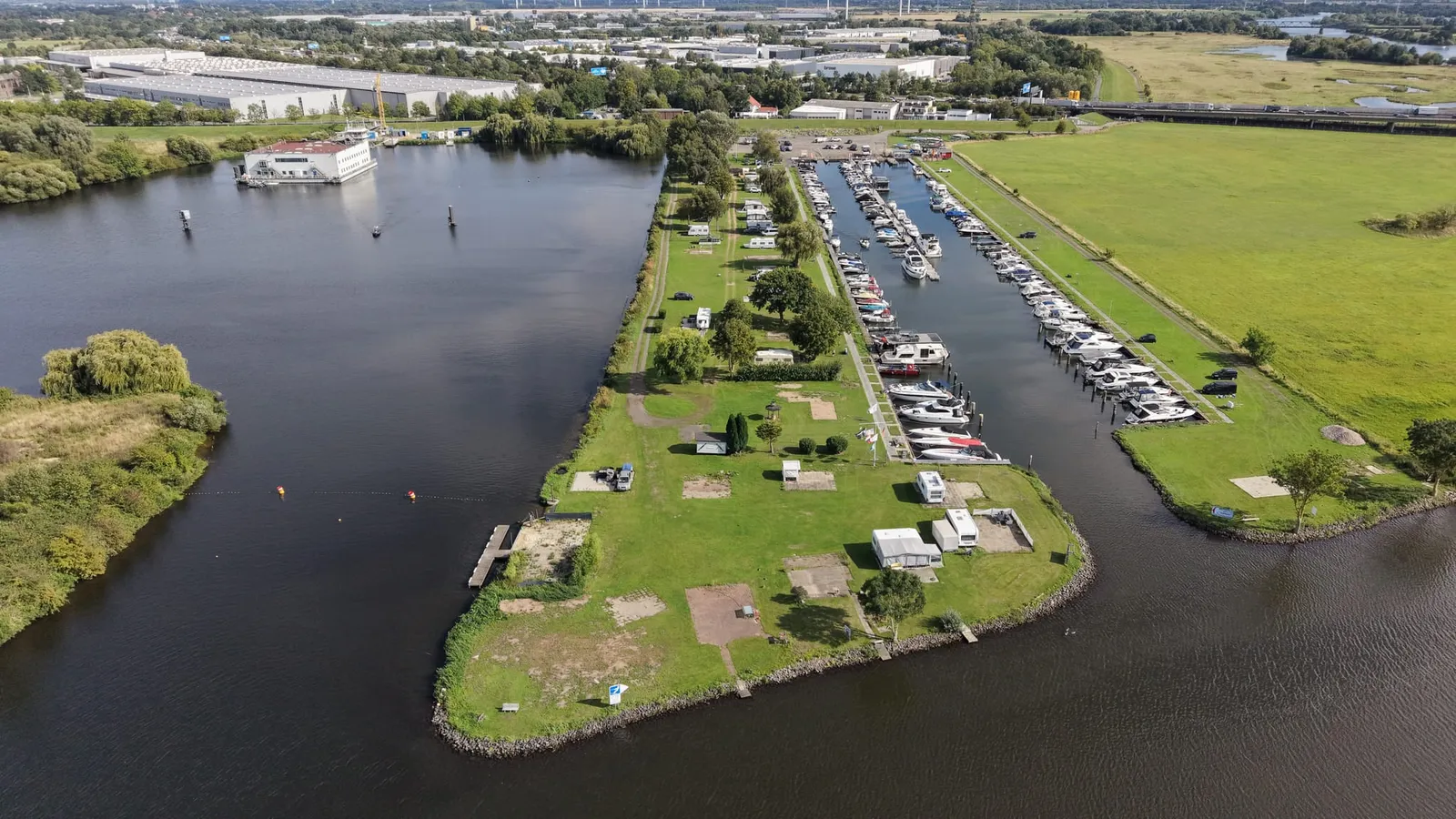 Luftaufnahme des Standorts in Bremen-Hemelingen: das Hafenbecken mit seinen Stegreihen zwischen Weser und Wiesen, dahinter das Gewerbegebiet an der A1